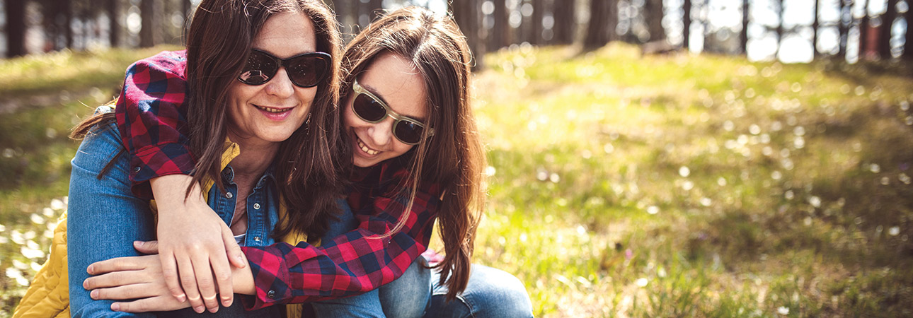Teen daughter sitting with and hugging mother in a field